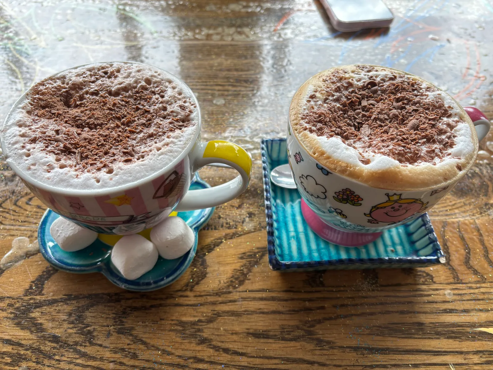 Two chai lattes in novelty Mr Men mugs with chocolate dusting and marshmallows
