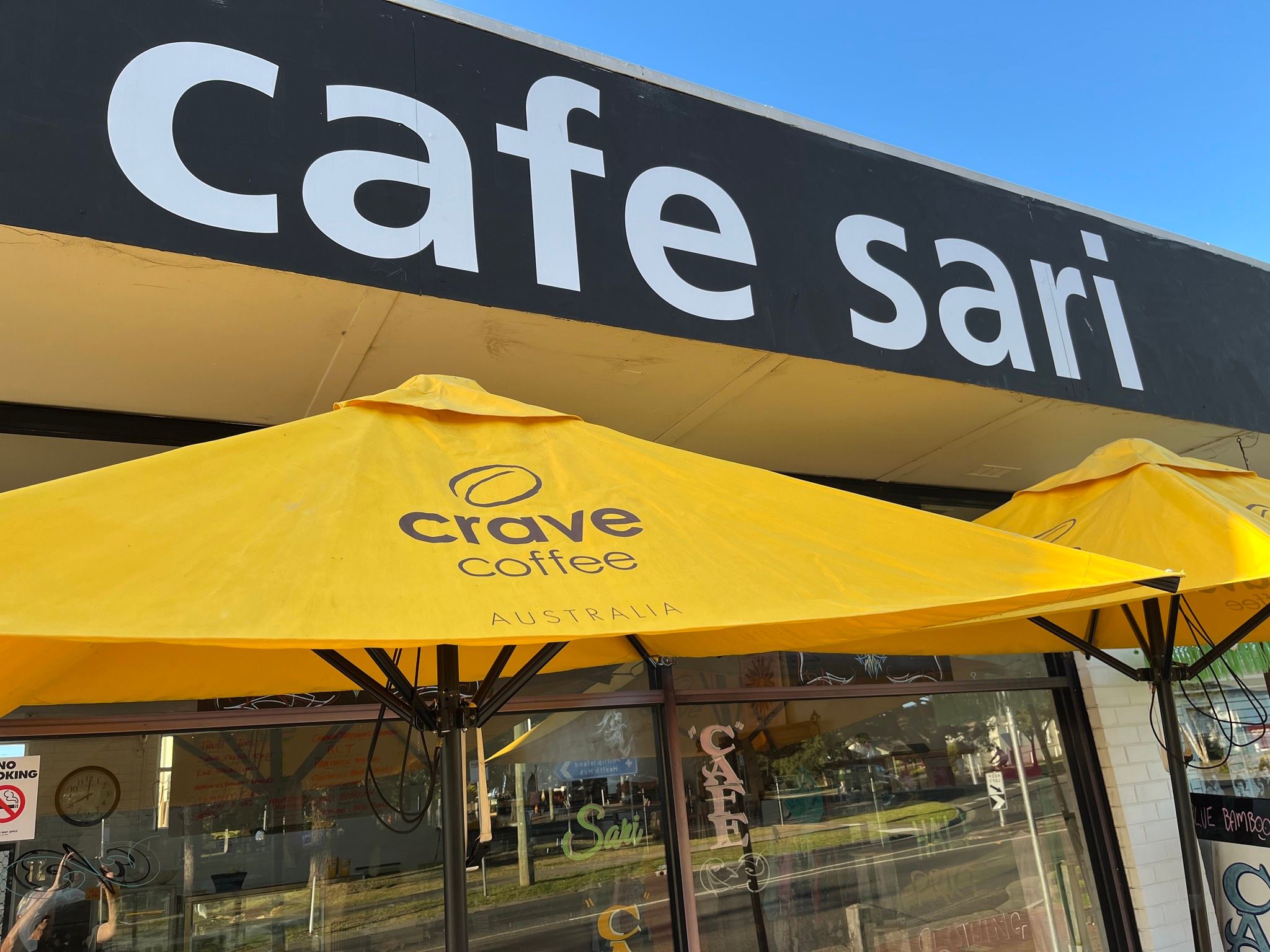 Cafe Sari storefront sign in white on black with yellow Crave Coffee umbrellas outside
